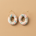 Pastelkleurige ovale oorbellen met open midden en goudkleurige ringetjes op beige achtergrond