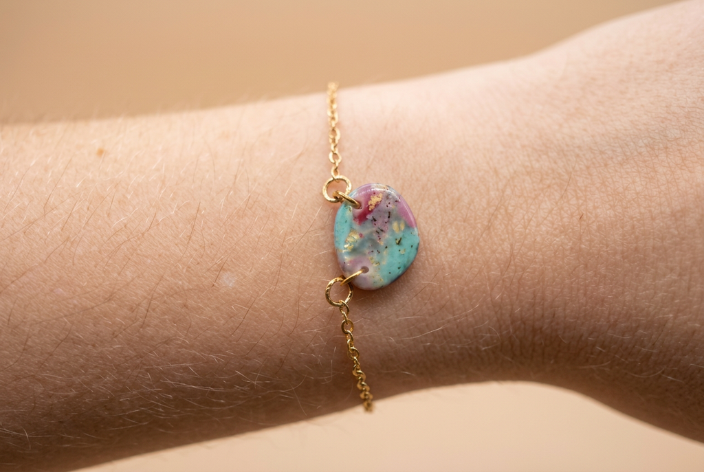 Goudkleurige armband met kleurrijk rond sierelement aan een pols tegen een rustige beige achtergrond