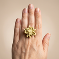 Licht geelgroene bloemring gedragen op een hand tegen een beige achtergrond