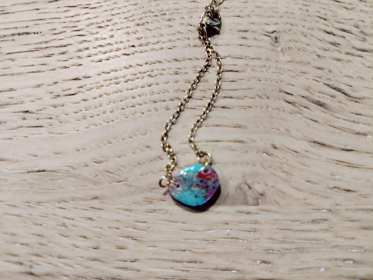 Goudkleurige schakelarmband met een kleurrijk rond sierelement op een houten tafel