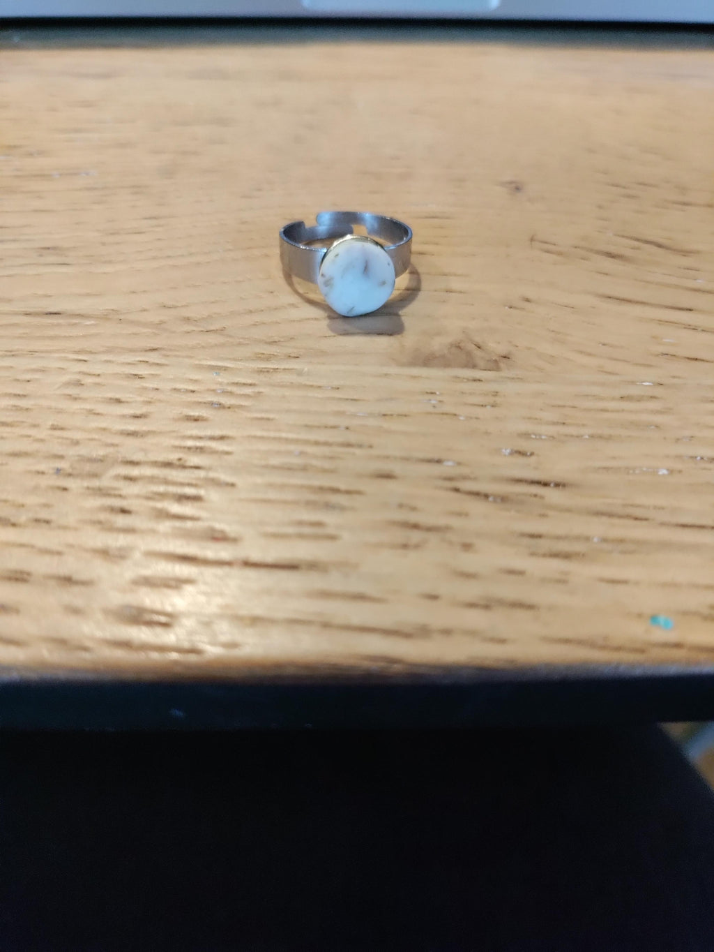 Zilverkleurige ring met brede band en licht rond sierelement op een houten tafel