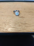 Zilverkleurige ring met brede band en licht rond sierelement op een houten tafel